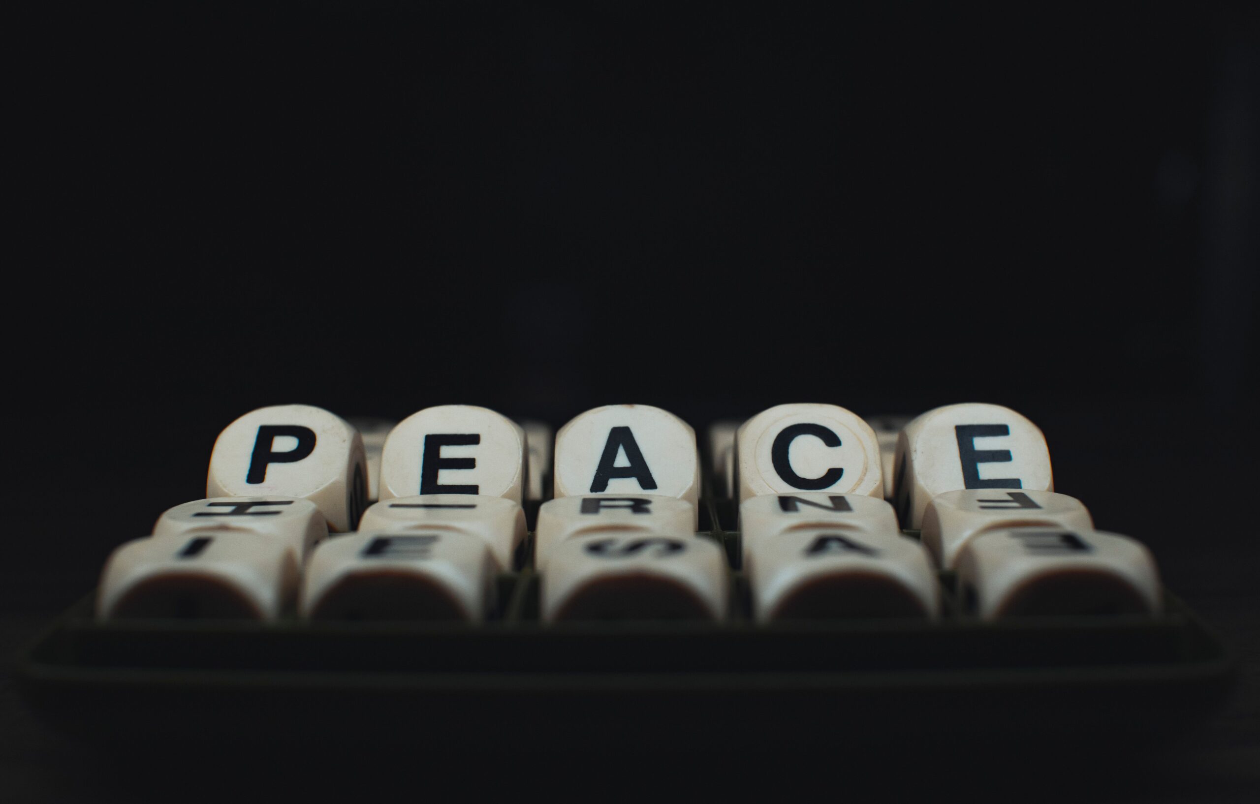 Close-up of wooden dice spelling 'Peace' on a black background, highlighting creativity and conceptual art.